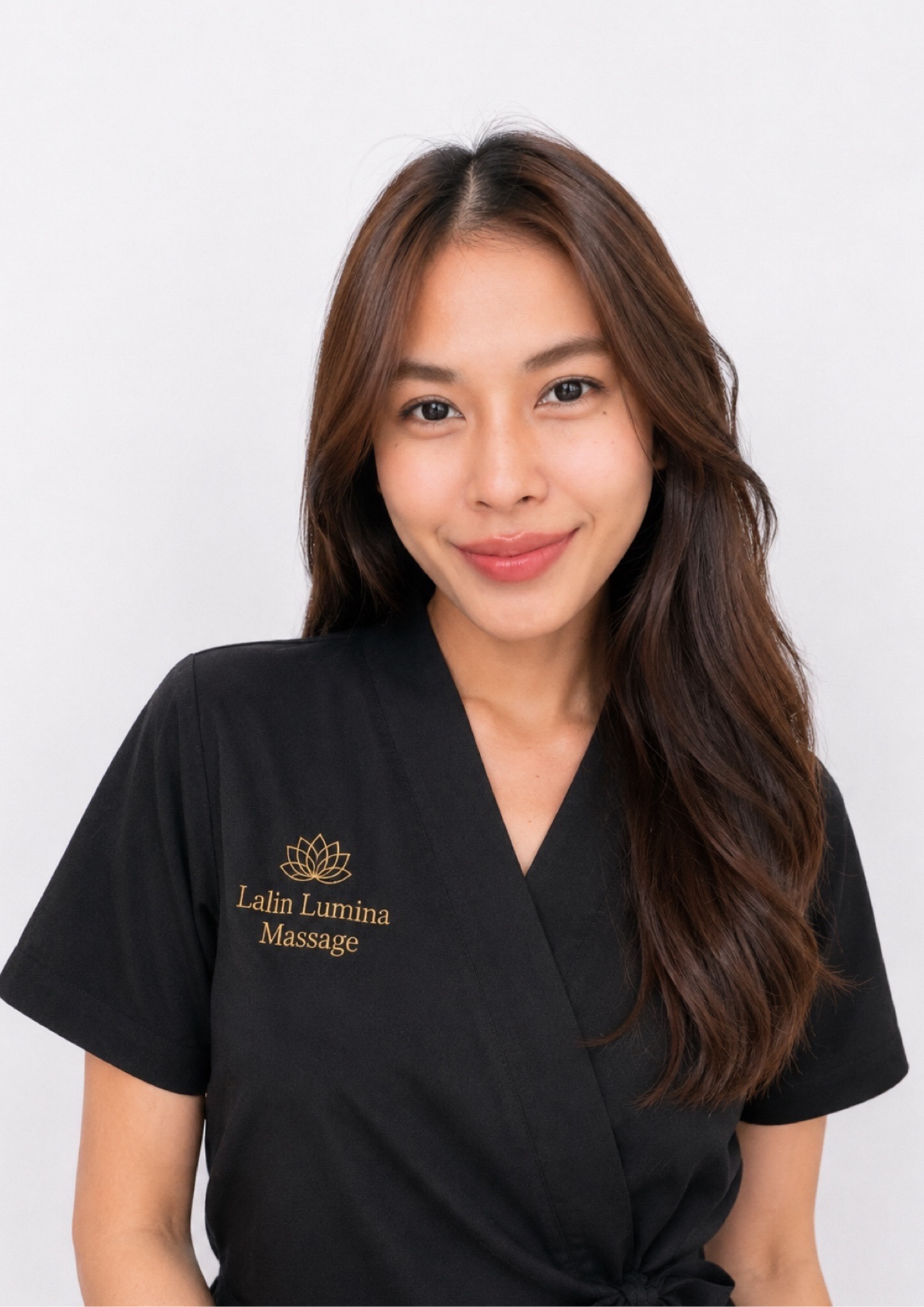 A woman with long hair, wearing a black spa outfit, is shown from the waist up. Therapist lalin lumina massage in bangkok