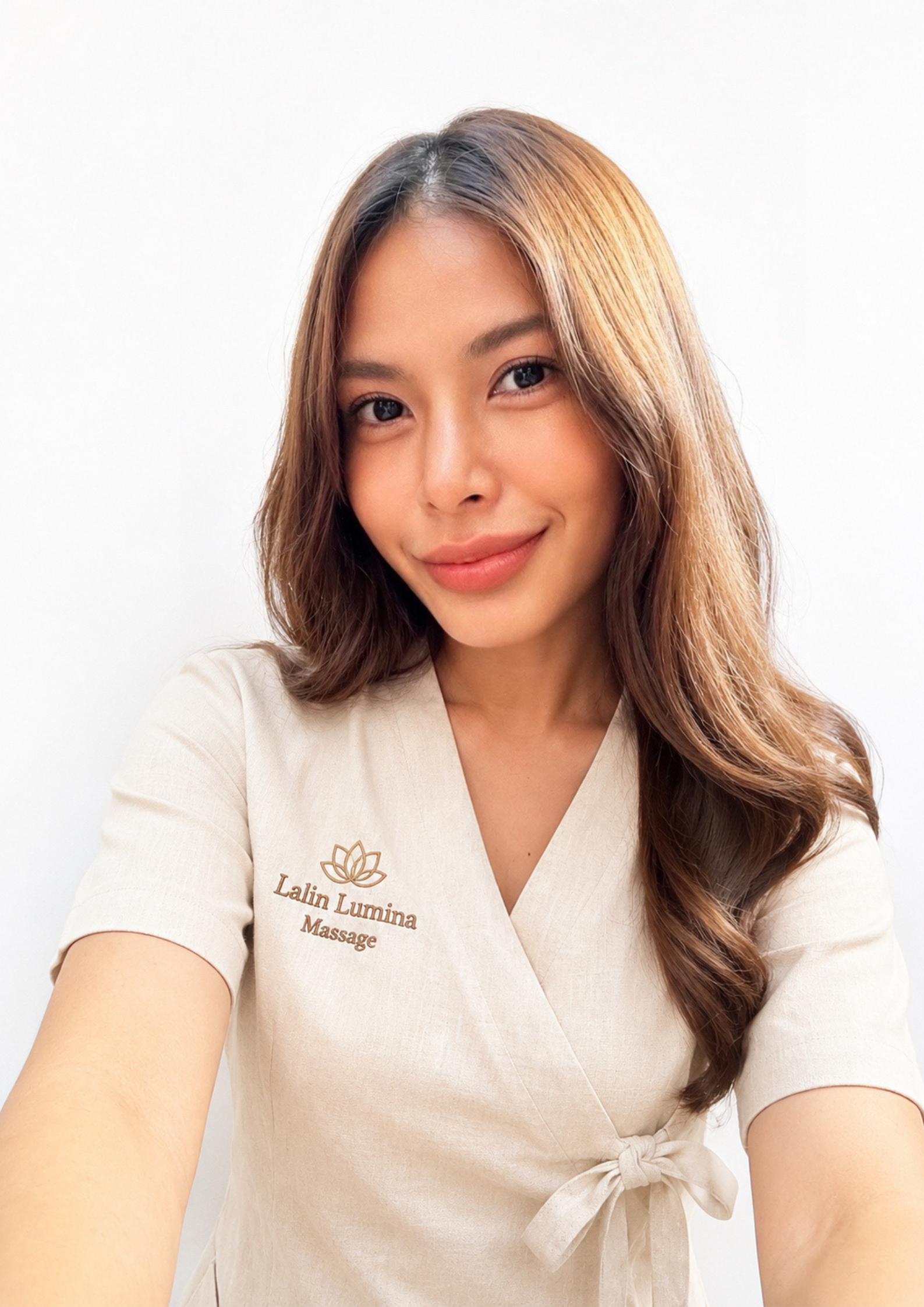 A woman with long hair, wearing a cream-colored spa outfit, is shown from the waist up. Therapist lalin lumina massage in bangkok